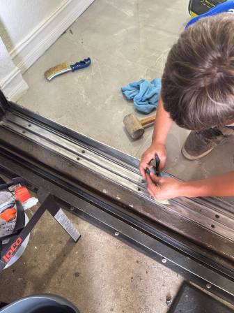 Technician using straightedge and measuring tools to inspect sliding door track for damage
