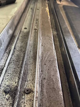 Extreme close-up macro shot showing deep grooves and pitting damage in aluminum track channel